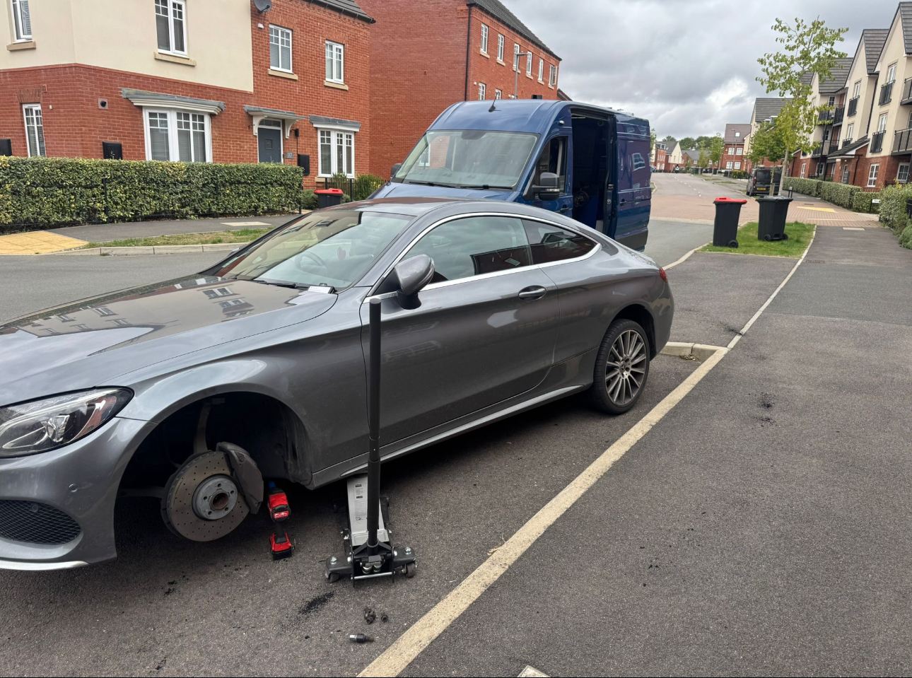 Car with its wheel removed on a residential street awaiting mobile tyre fitting